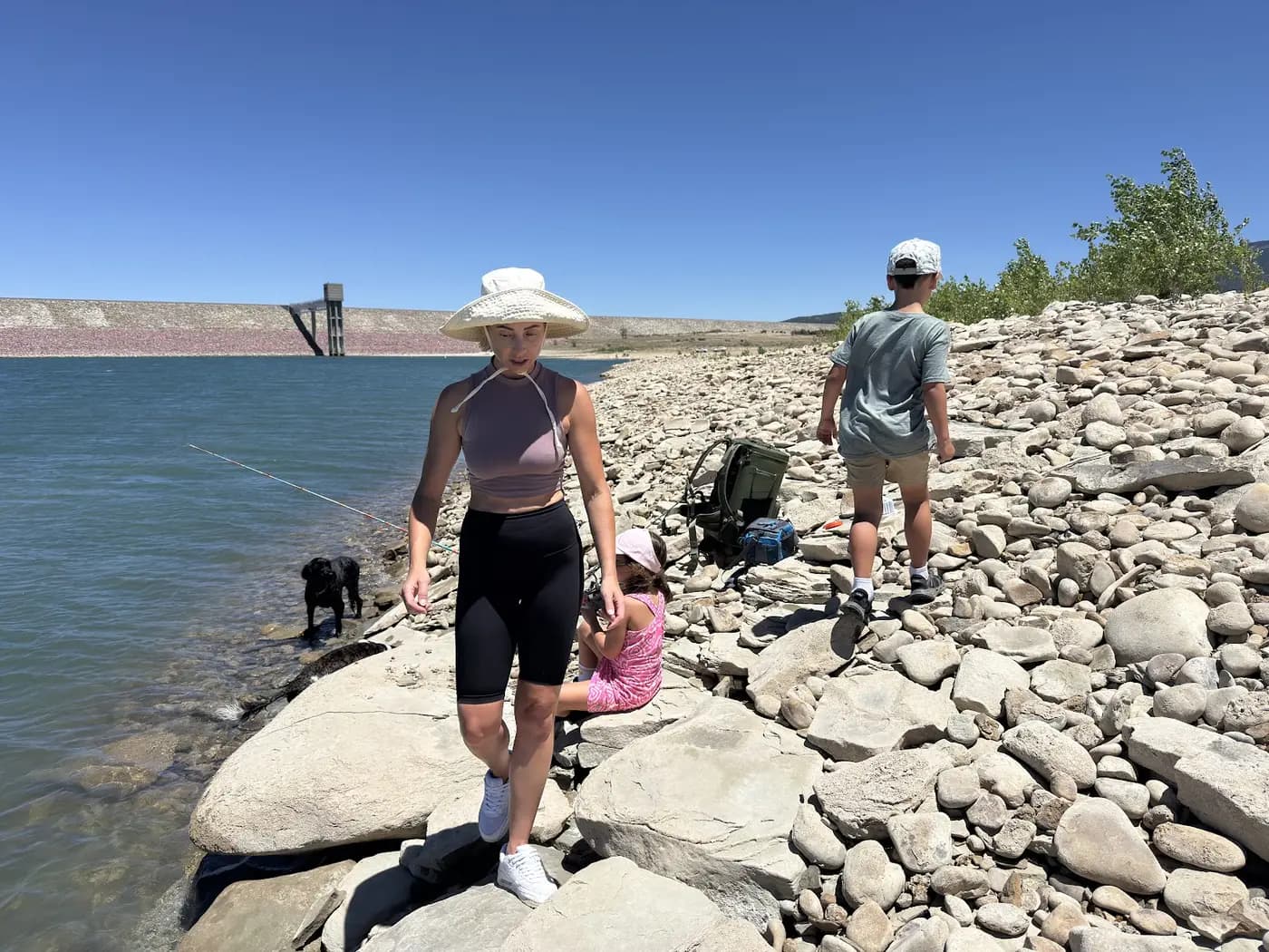 A fishing day on a rocky reservoir shore, the kids picking their spots while one of the dogs tests the water